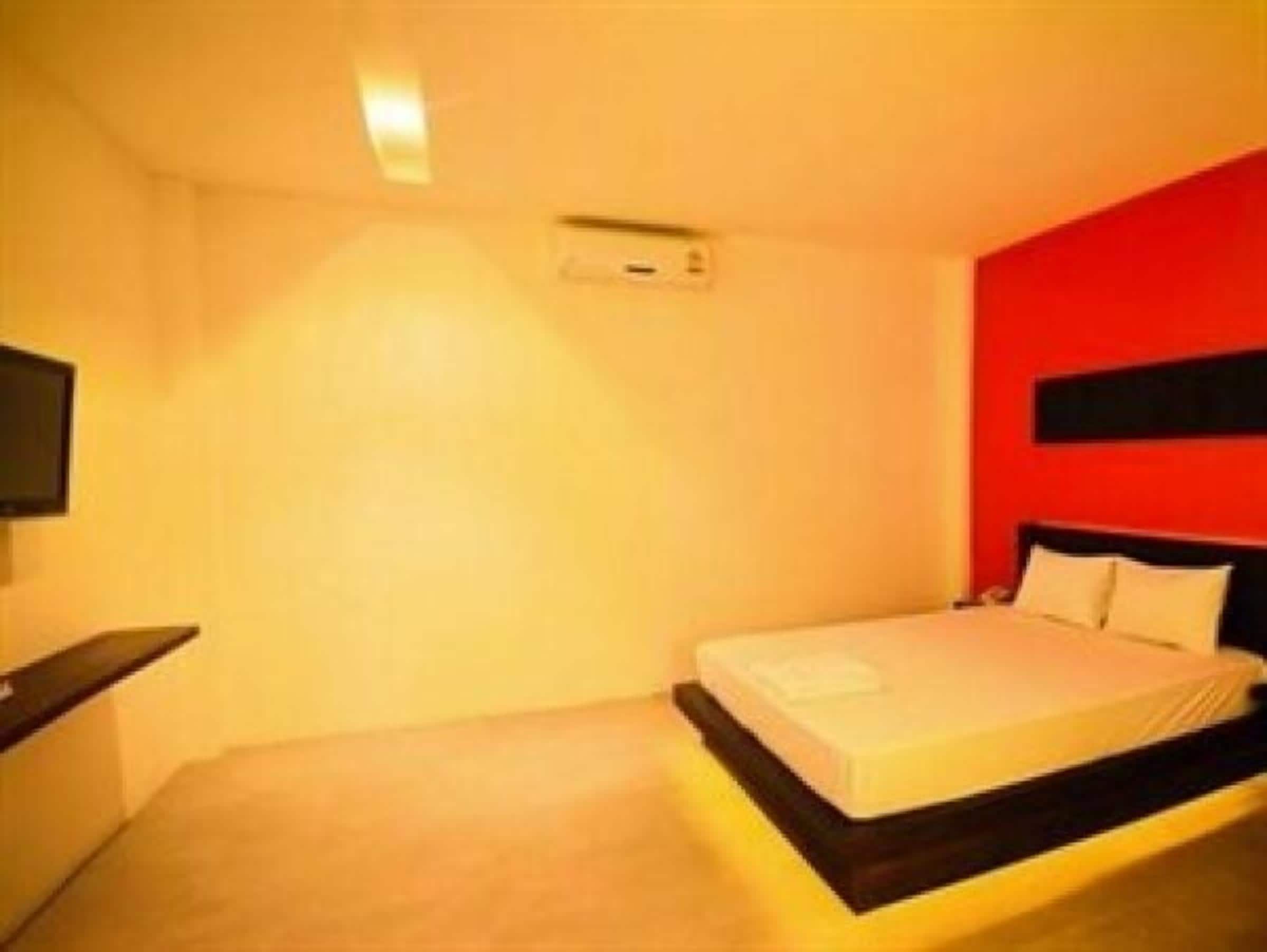 Una habitación de hotel con cama, mesita de noche y televisión instalada en la pared.
