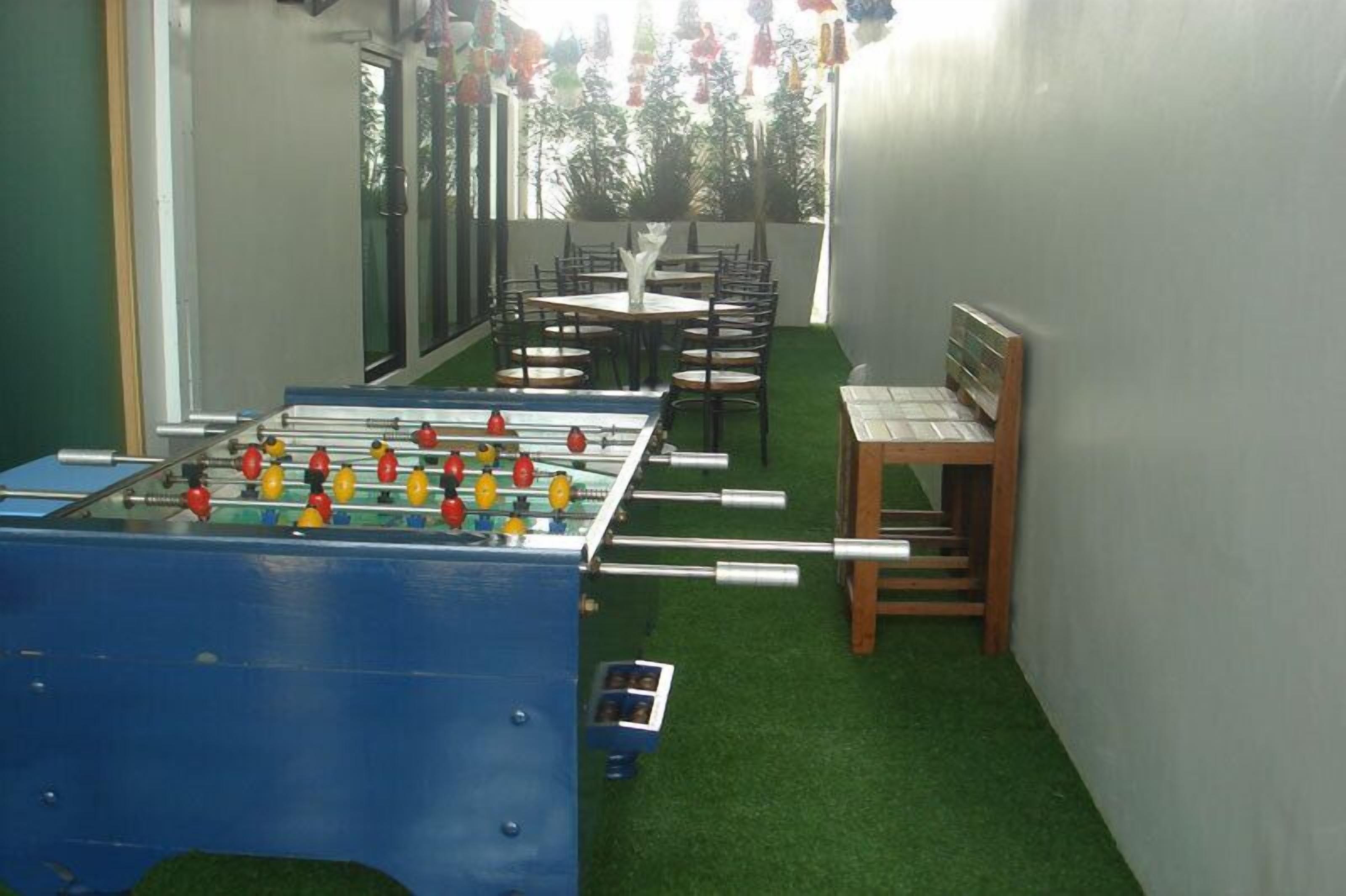 A room with a foosball table, a small wooden bench, and a dining area with tables and chairs.