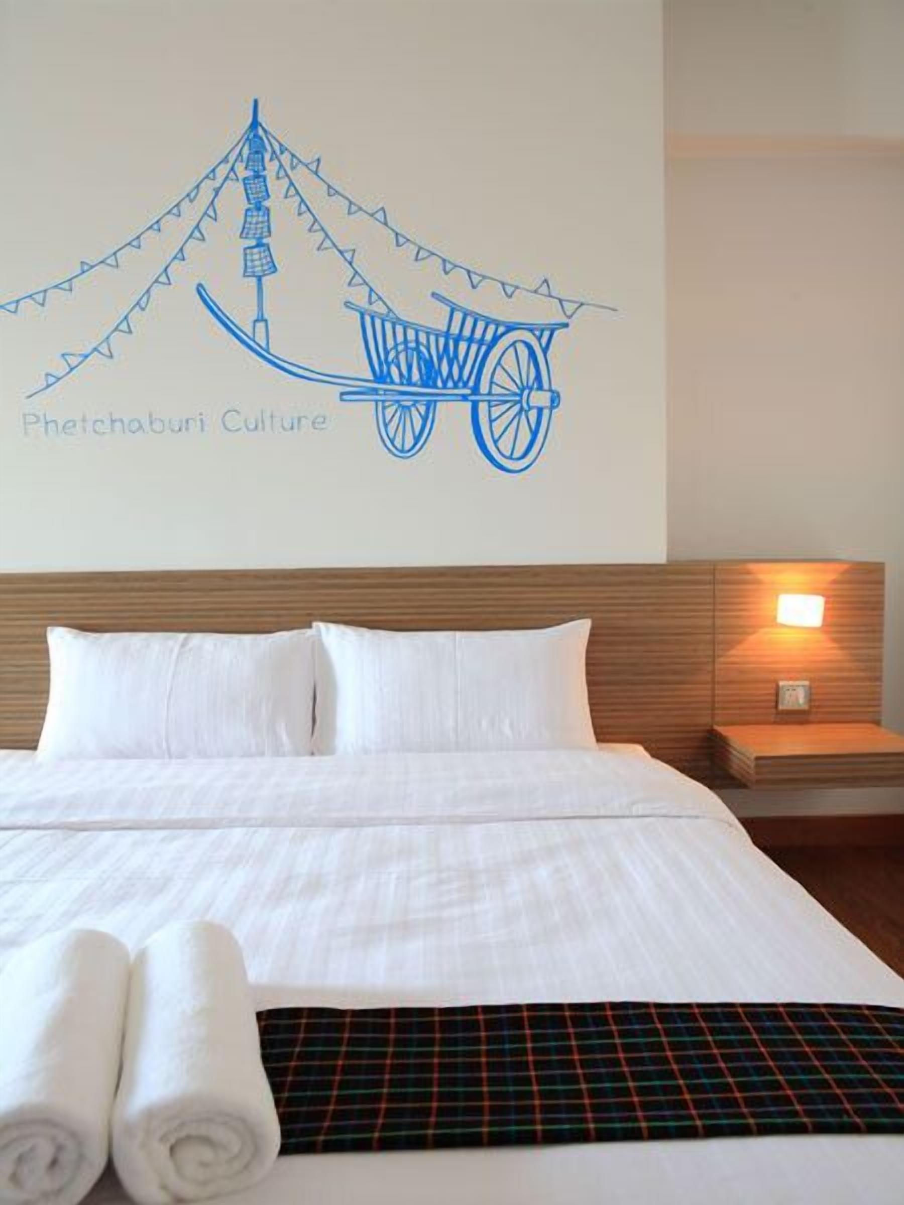 A hotel room with a bed, pillows, a blanket, and a wall decoration depicting a traditional carriage.