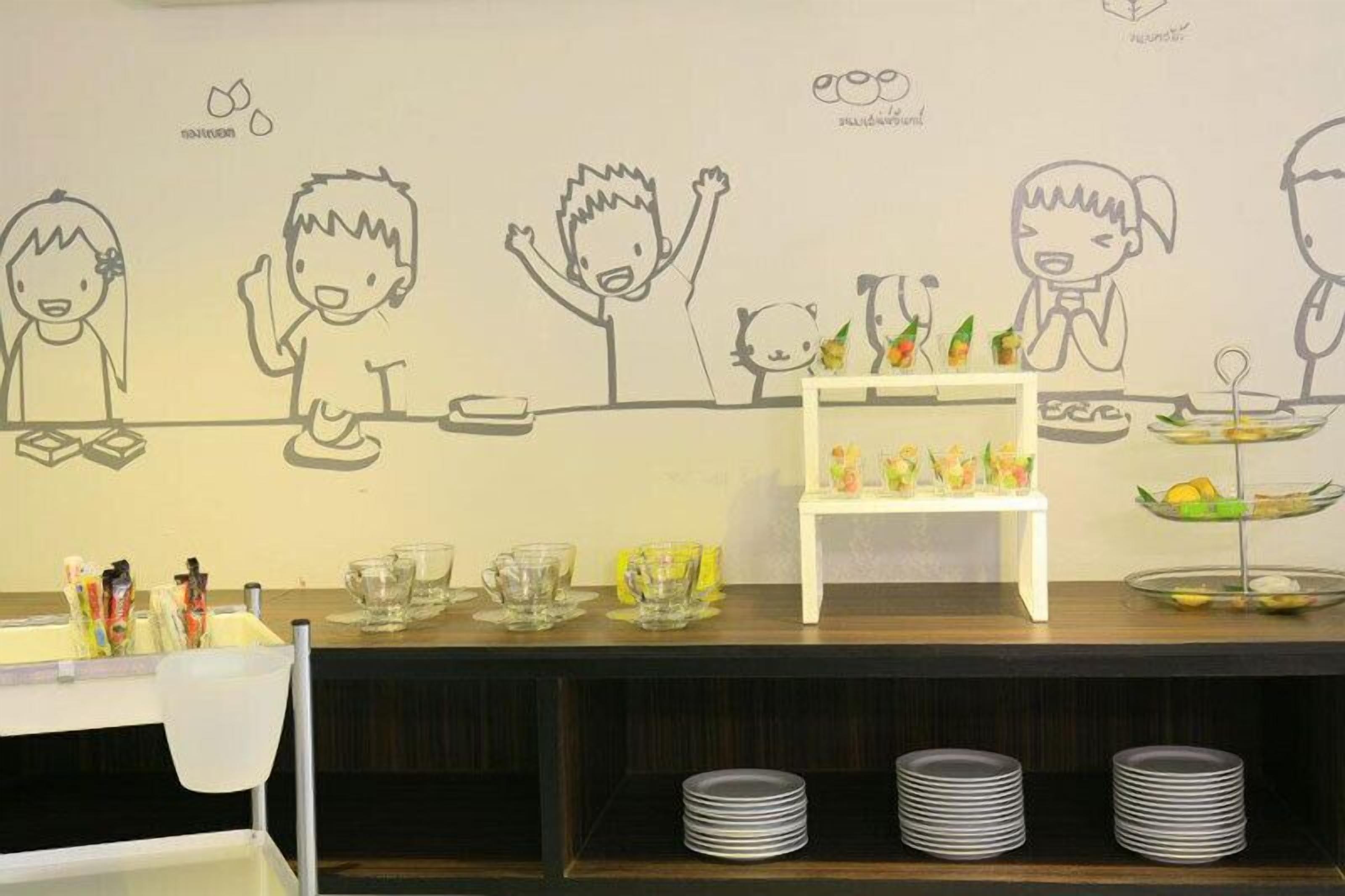 A dining area with a counter, children's drawings on the wall, and a small shelf with food items.