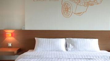 Habitación de hotel con cama, mesita de noche con lámpara y decoración de pared que muestra un carrito con el texto 'Kanom-Whan'.