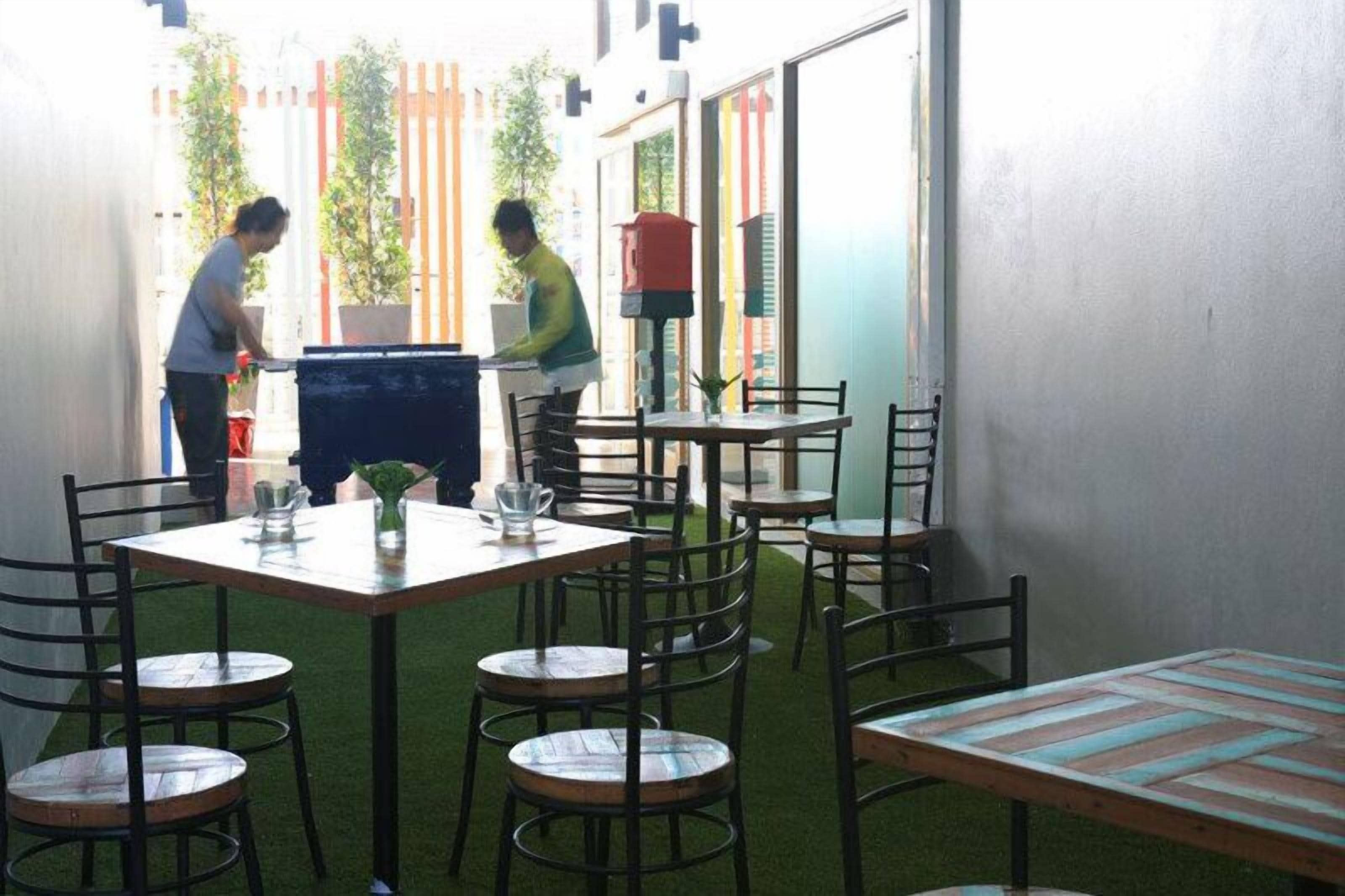 Un espace extérieur aménagé pour les repas, avec des tables et des chaises, un petit jardin et un bâtiment en arrière-plan.