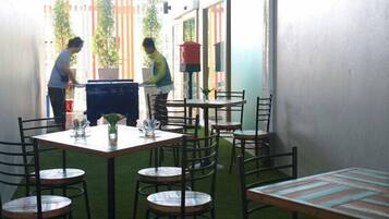 Un espace extérieur aménagé pour les repas, avec des tables et des chaises, un petit jardin et un bâtiment en arrière-plan.