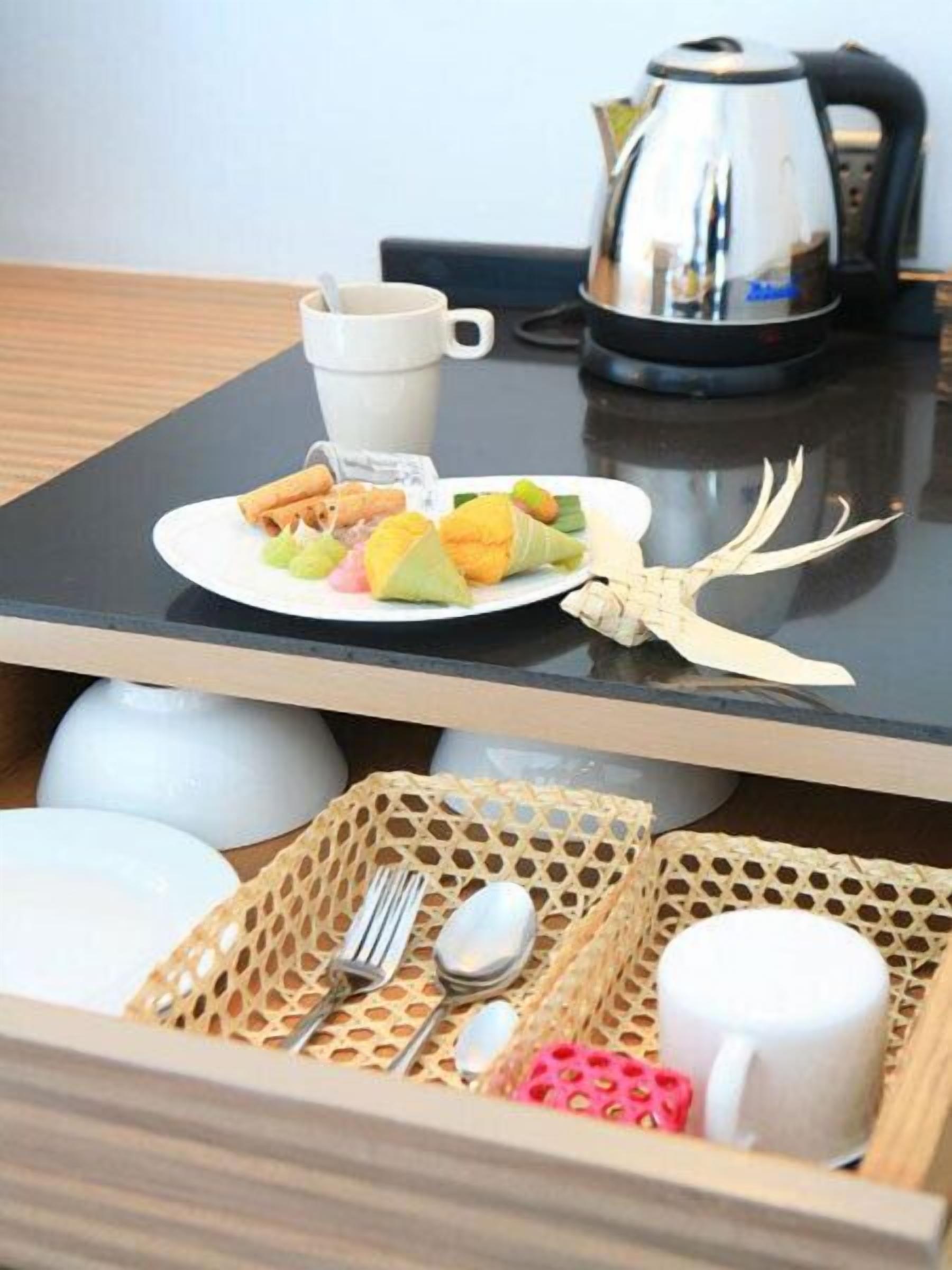 Una mesa de comedor con un plato de comida, una taza, un hervidor y una cesta con utensilios.