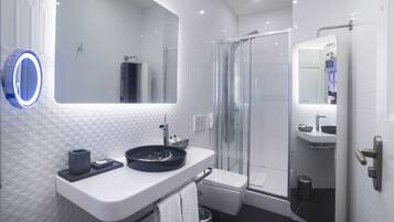 A modern bathroom with a glass-enclosed shower, a white sink with a black basin, and a large mirror with a circular light.