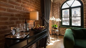 A room with a brick wall, a window with a view of buildings, a green sofa, a table with a lamp and a bowl of fruit, and a potted plant. - Régie Ottoman Istanbul (Istanbul)