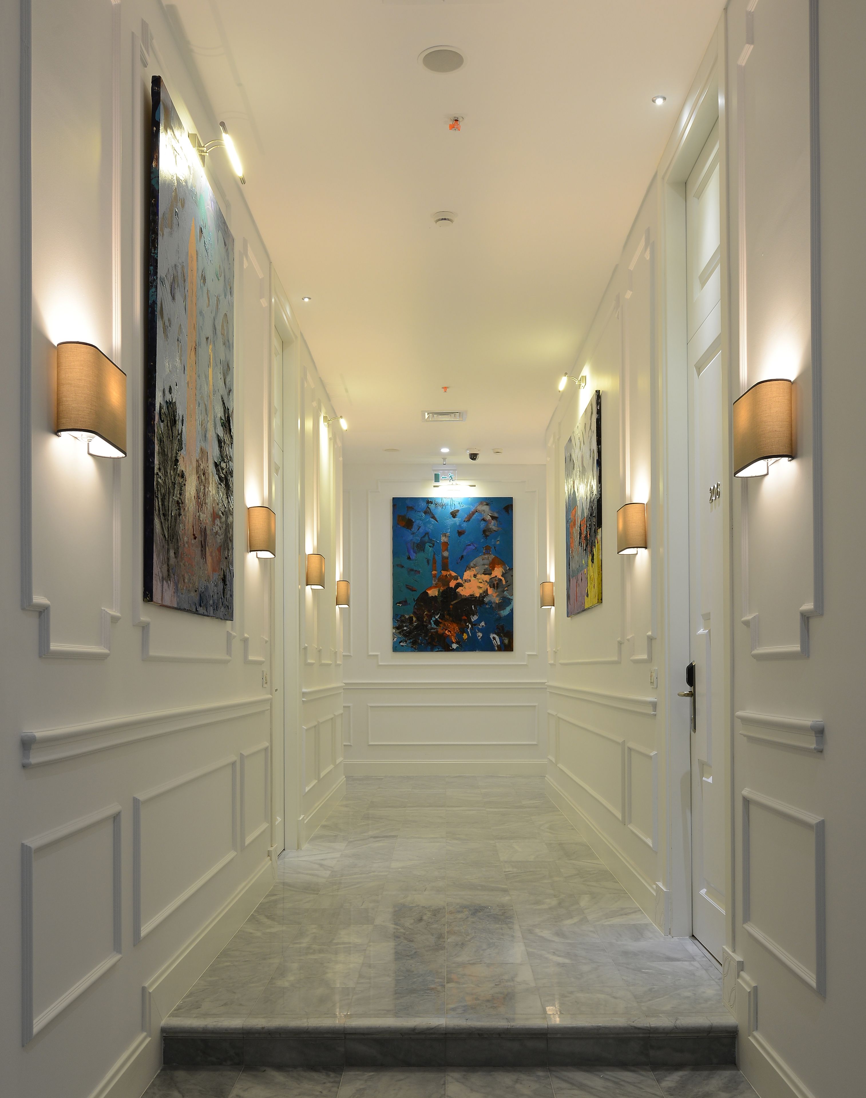 A hallway with white walls, marble flooring, and artwork on the walls.