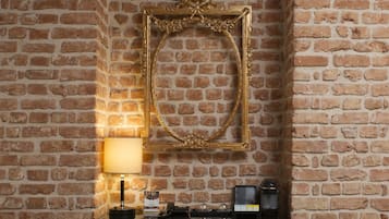 A brick wall with a gold-framed mirror and a small table with a lamp, books, and a radio.