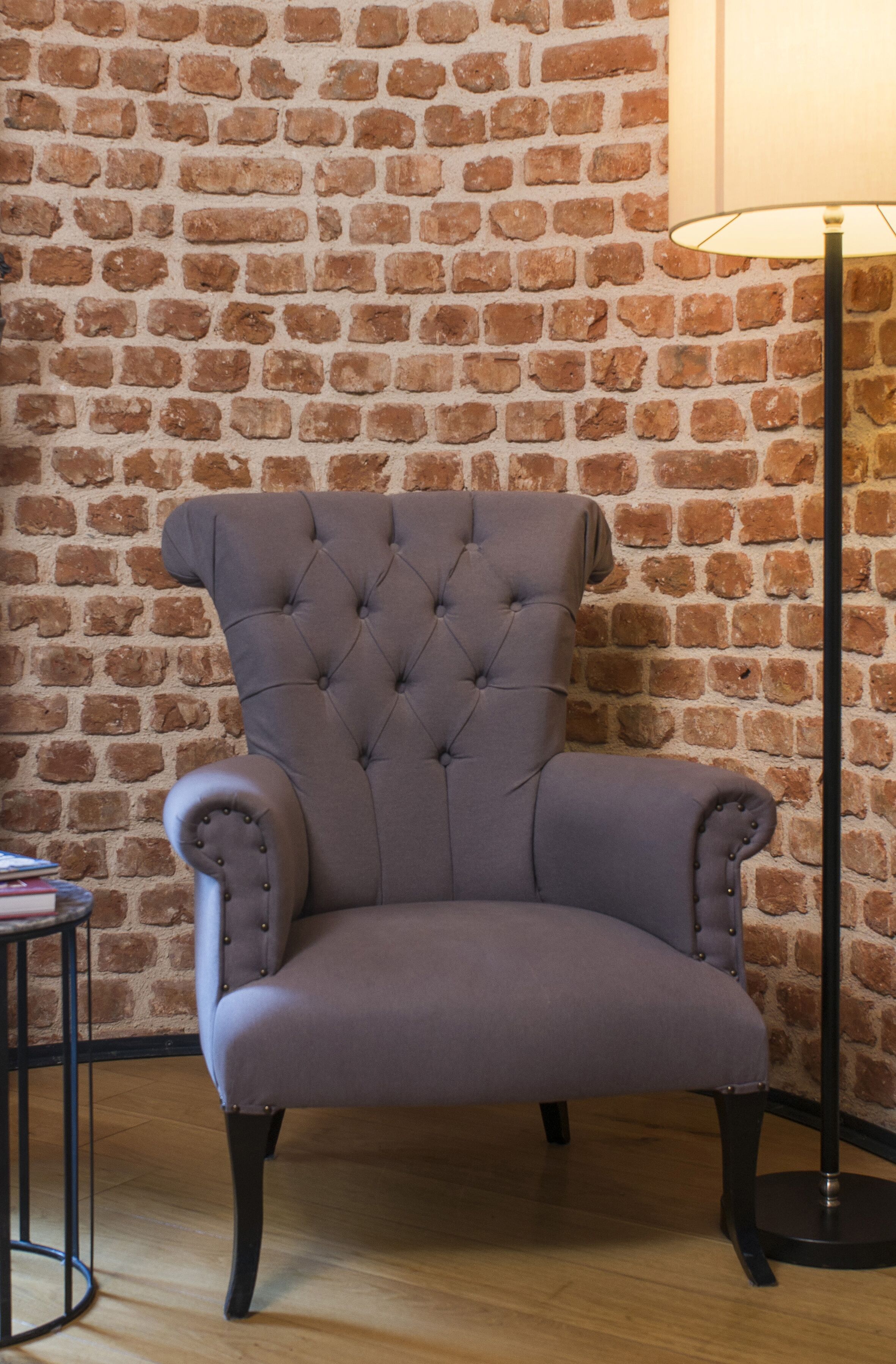A tufted armchair with a high back, positioned against a brick wall.