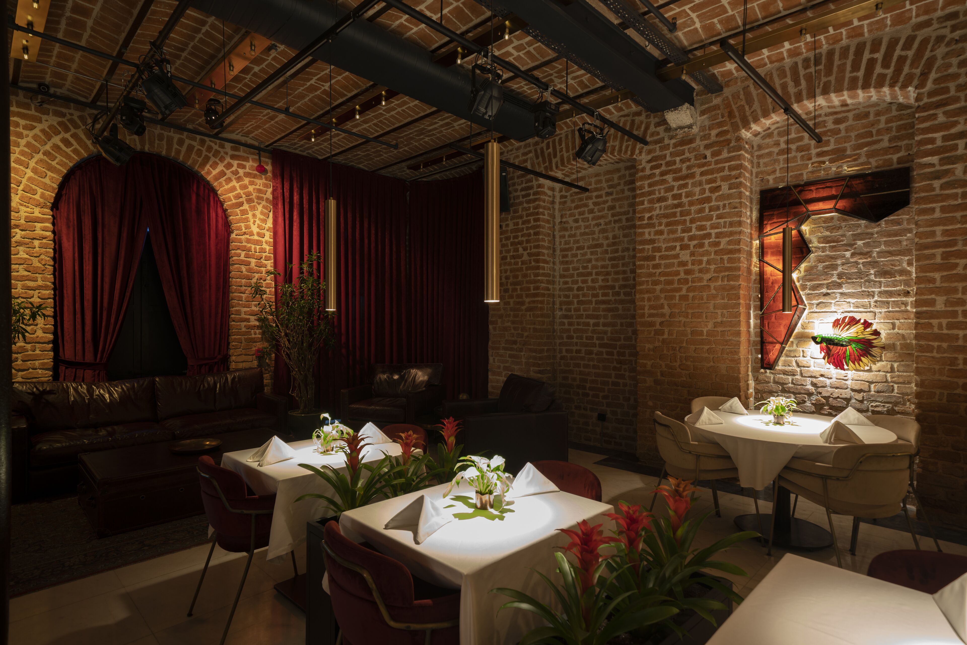 Un restaurant aux murs de briques, aux rideaux rouges et aux tables dressées pour le dîner.
