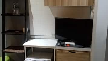 A compact room with a white desk, a small refrigerator, a TV, and a wooden cabinet.