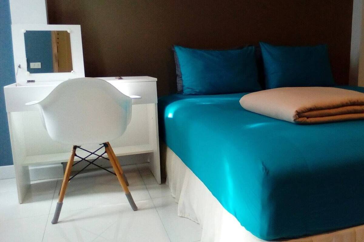 Une chambre à coucher avec un lit, une chaise blanche, un bureau et un miroir.