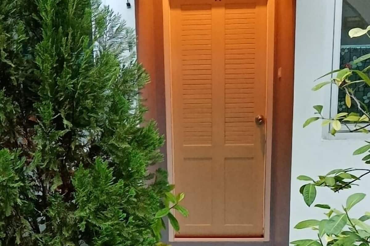 Une porte en bois, avec un petit porche et des marches menant à l’entrée, entourée de plantes en pot et d’un chemin de pierres.