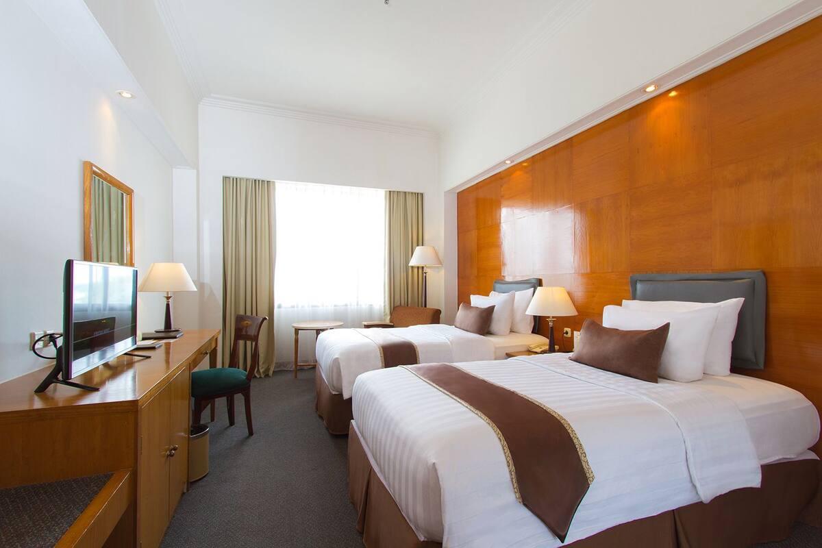 Une chambre d’hôtel avec deux lits, un bureau avec une télévision, une chaise et une petite table.