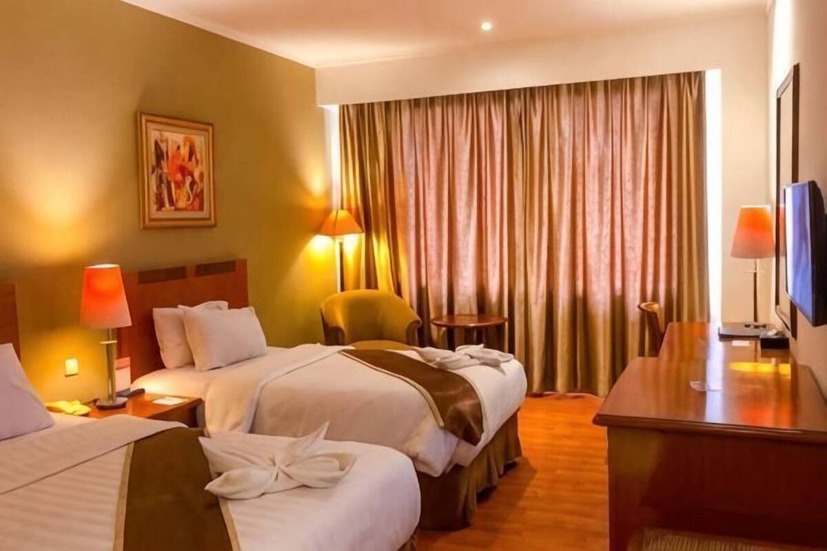 Une chambre d’hôtel avec deux lits, un bureau, une chaise, une télévision et une fenêtre avec des rideaux.