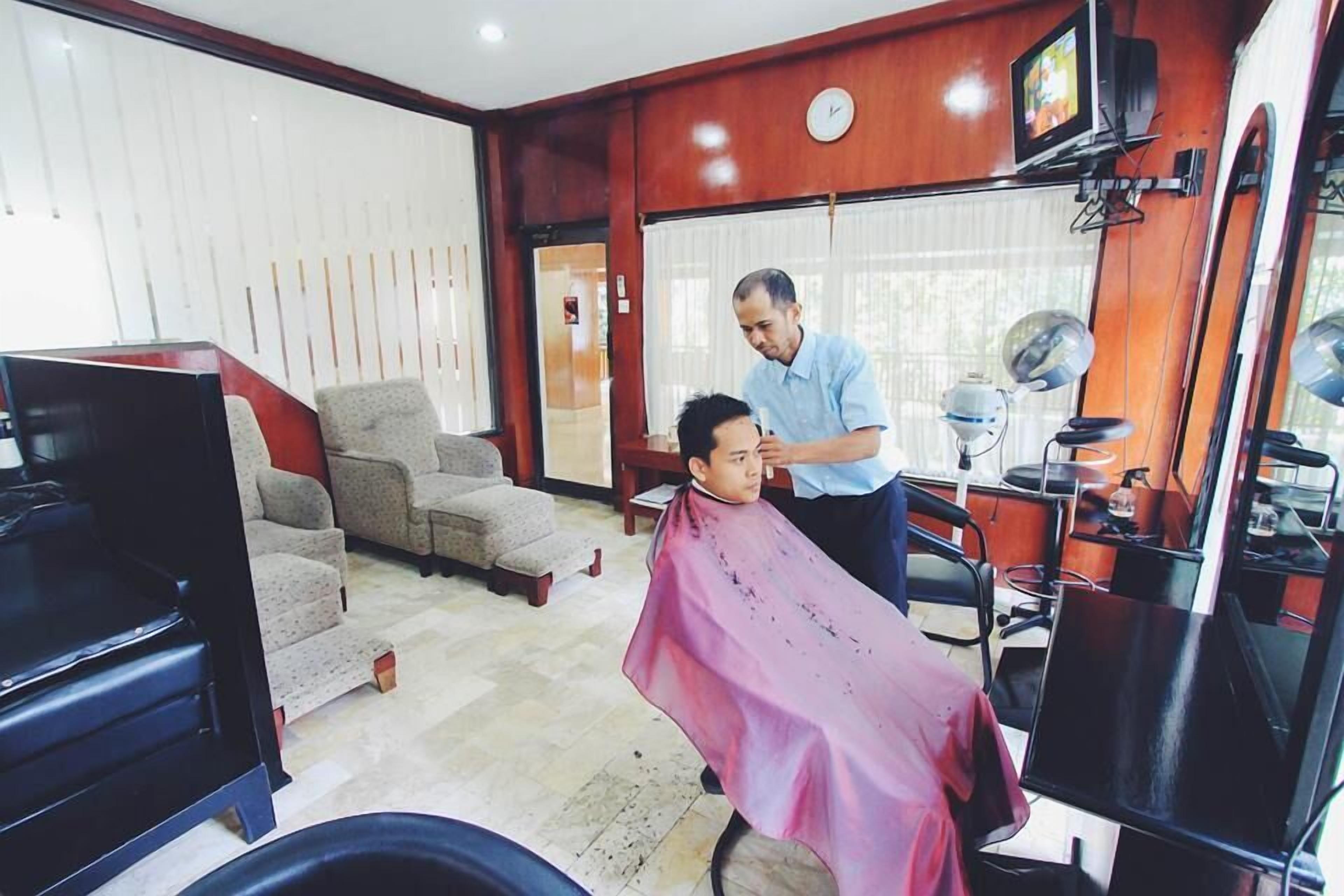 A barber shop with a waiting area, a barber chair, a television, and a mirror.