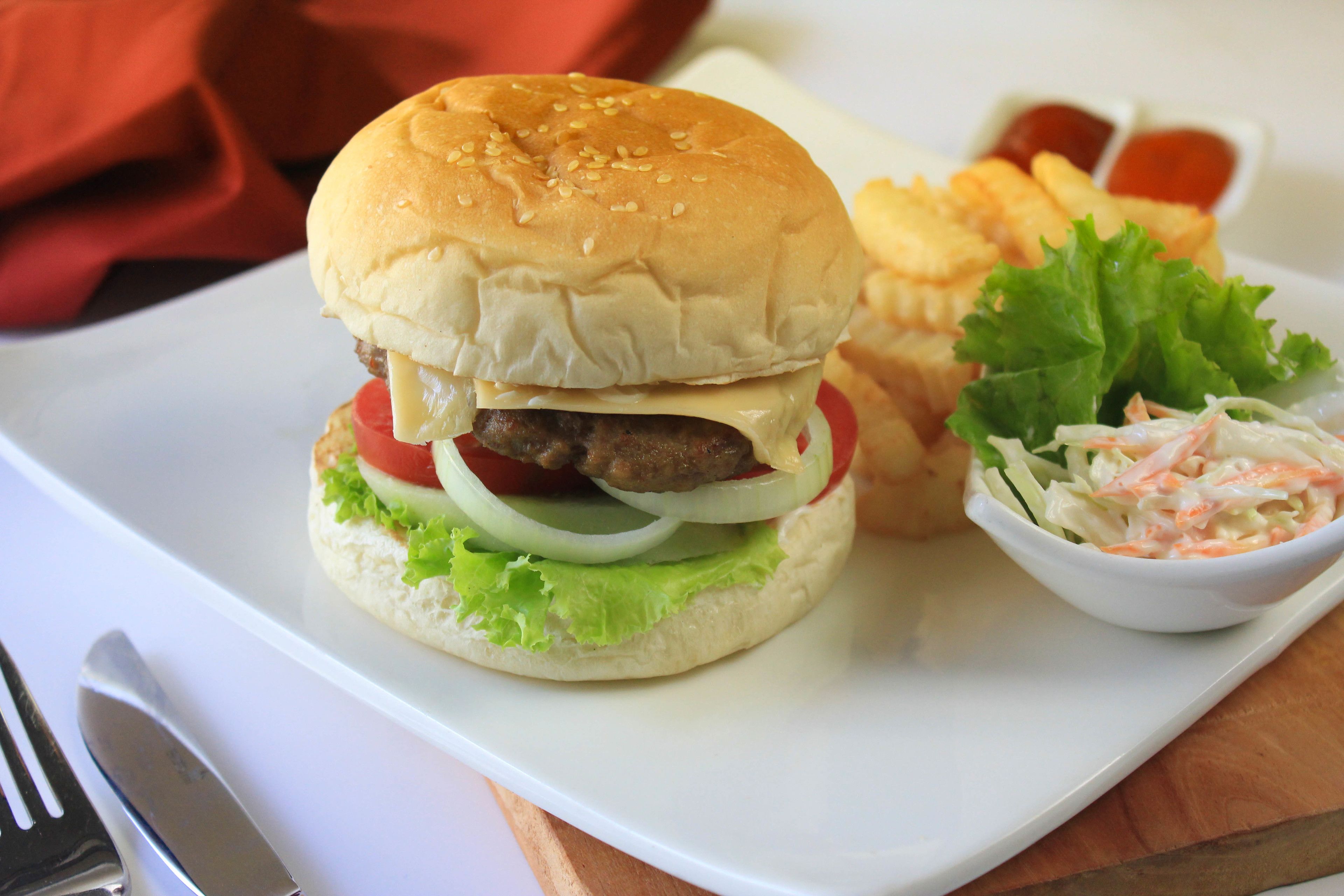 Hamburguesa con lechuga, tomate y cebolla, acompañada de papas fritas y ensalada de col, sobre un plato blanco.