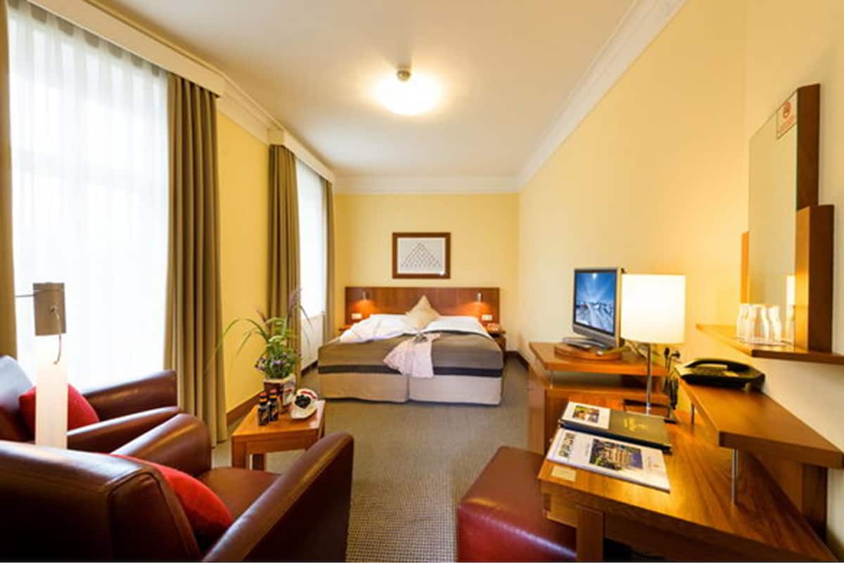 A hotel room with a bed, a desk, a chair, a TV, and a window with curtains.