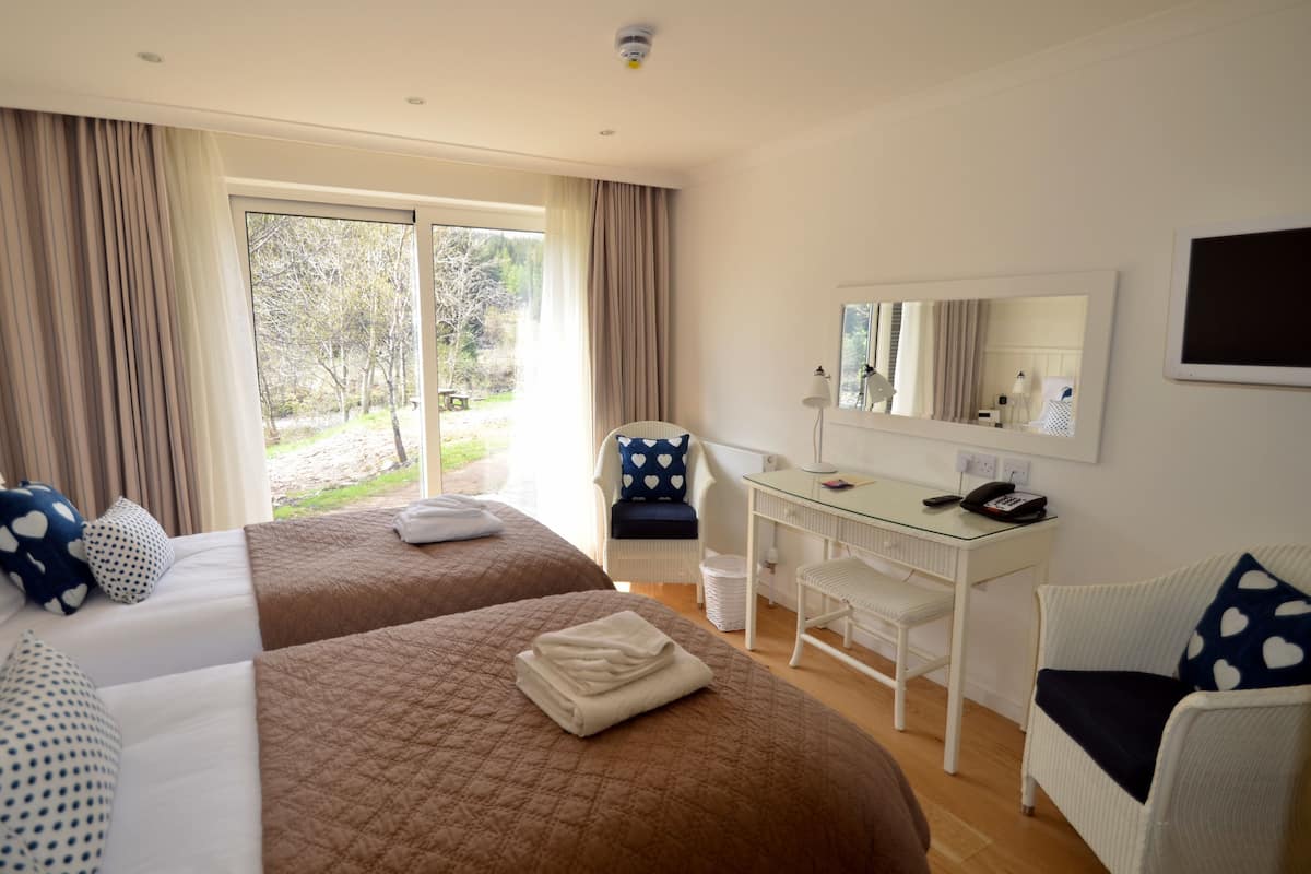 Habitación de hotel con dos camas, un escritorio, una silla, un espejo y vistas al exterior.