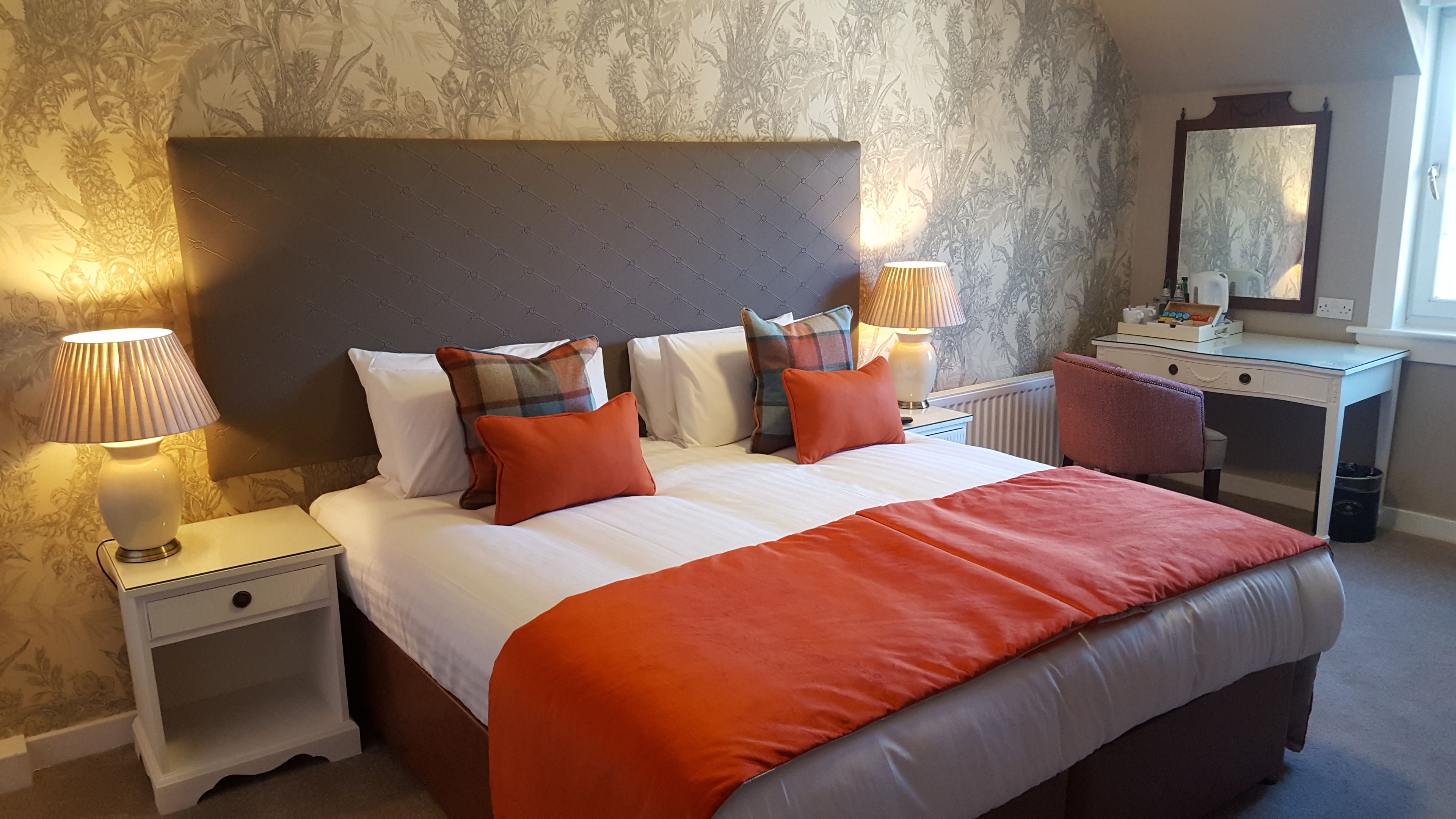 A hotel room with a large bed, two bedside tables, a desk, and a mirror.