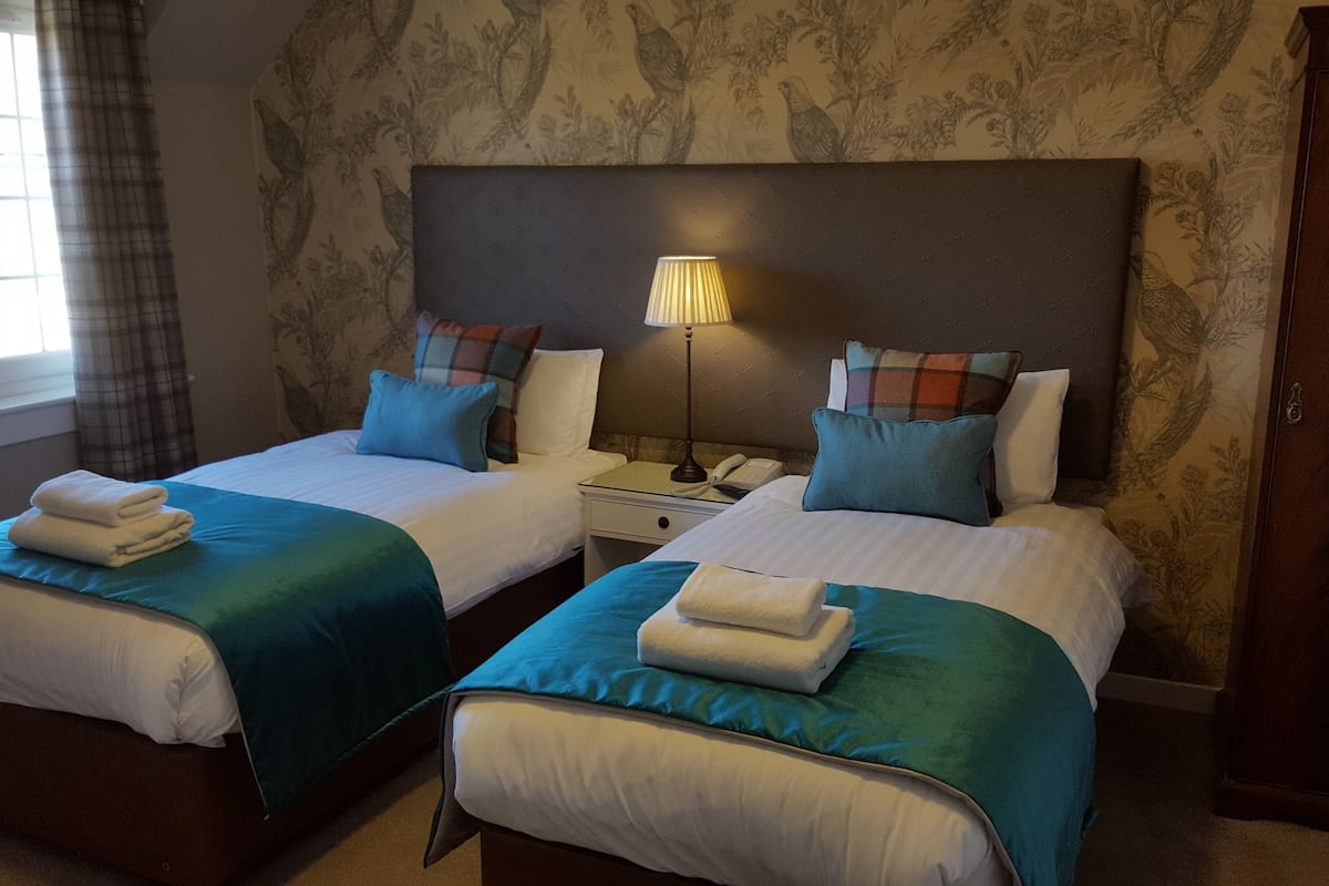 Una habitación de hotel con dos camas, cada una con una colcha azul y blanca, y una mesita de noche con una lámpara entre ellas.