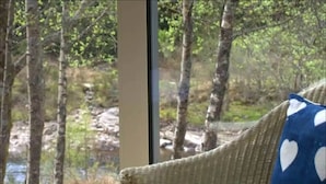 A room with a large window offering a view of a forested area and a stream. - Bridge of Orchy Hotel (Bridge of Orchy)