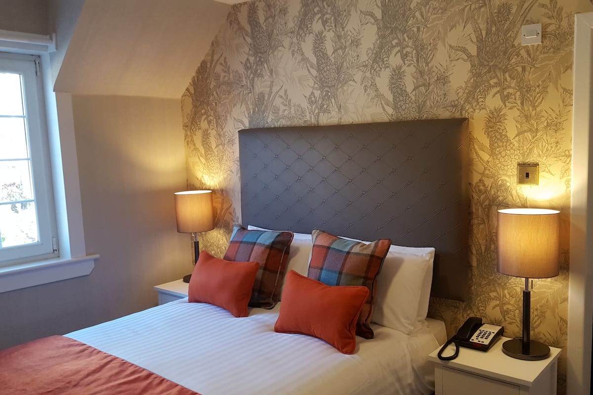 Habitación de hotel con una cama, dos lámparas de noche, un teléfono y un ventanal.
