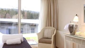 A hotel room with a bed, a chair, a lamp, and a view of a body of water and trees.
