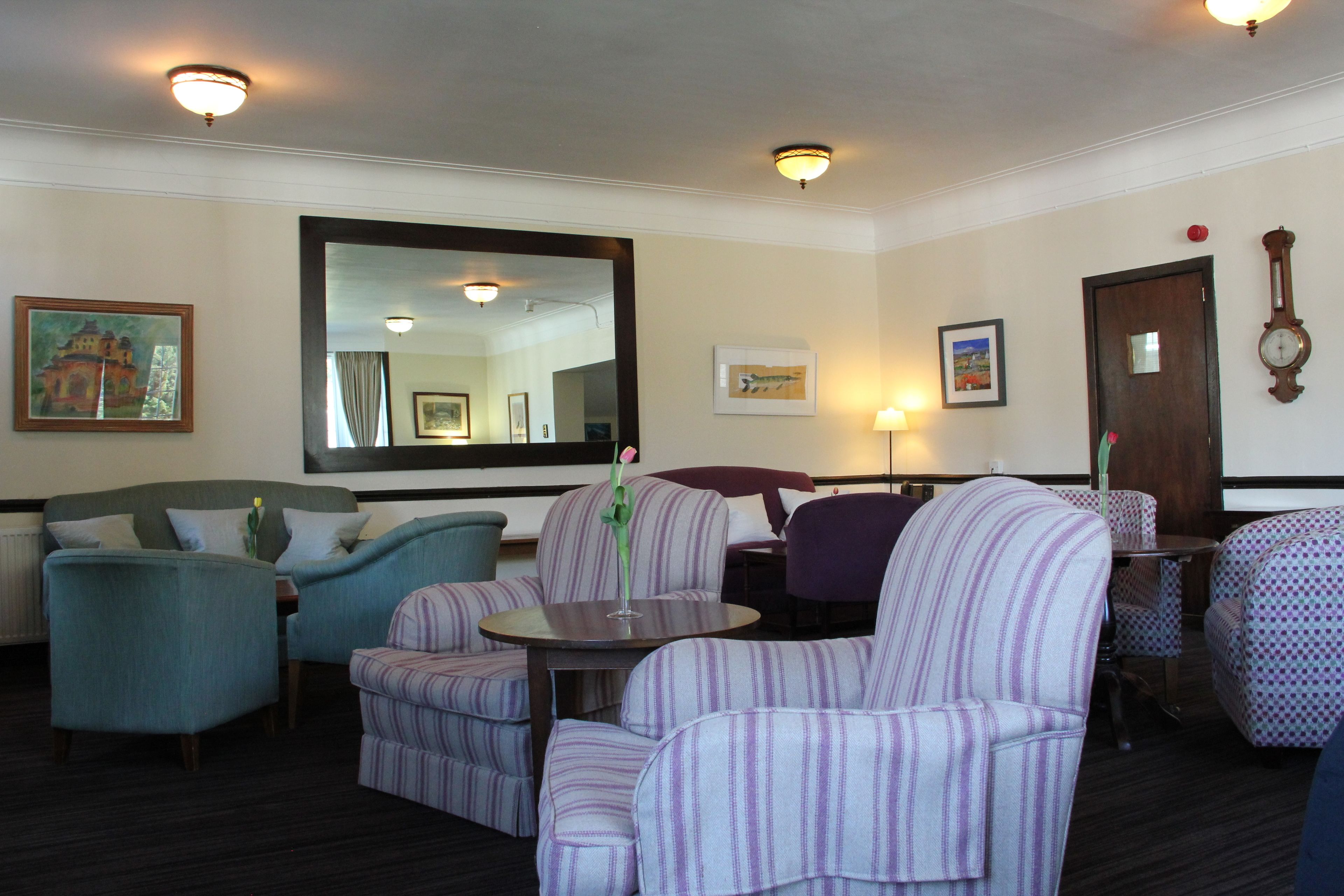 Un vestíbulo de hotel con sillones a rayas, una mesa redonda y un espejo grande.
