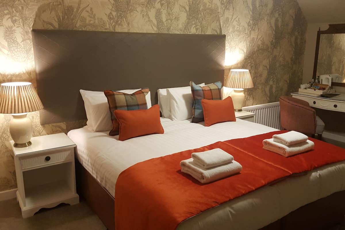 Habitación de hotel con una cama grande, dos mesitas de noche con lámparas, un escritorio con espejo y un radiador.