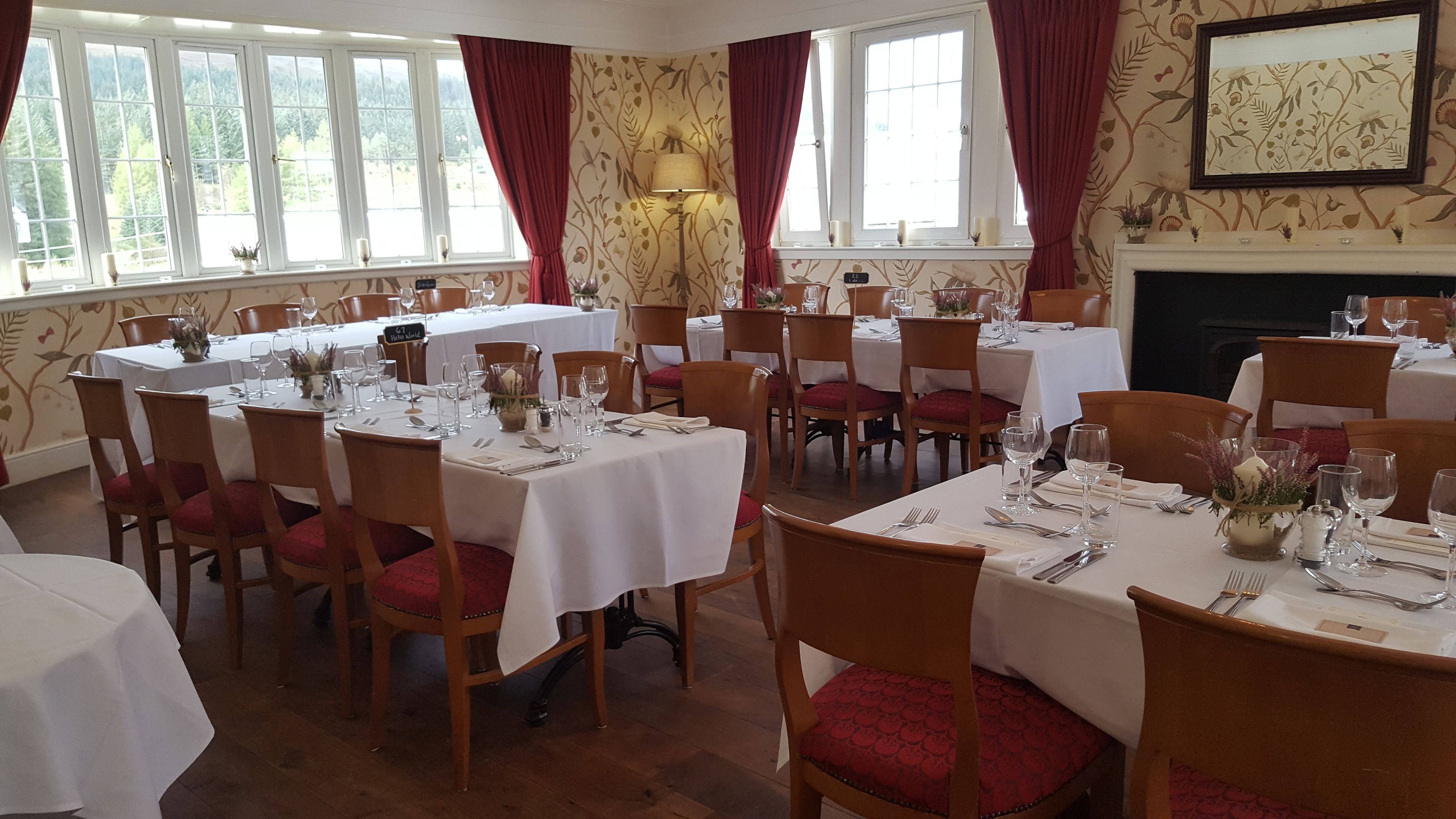 A dining area with multiple tables set for a meal, wooden chairs, and a fireplace in the background.