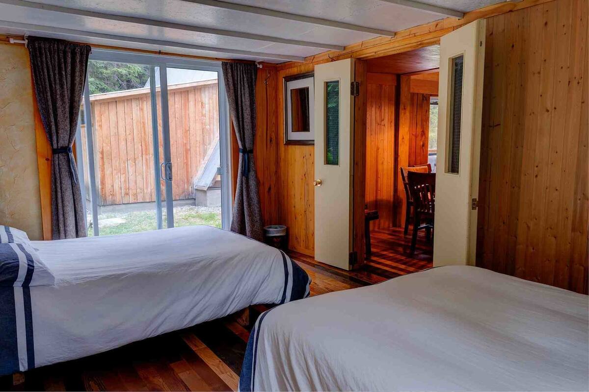 Ein Zimmer mit zwei Betten, Holzwänden, einem Fenster und einer Tür zu einer Treppe.