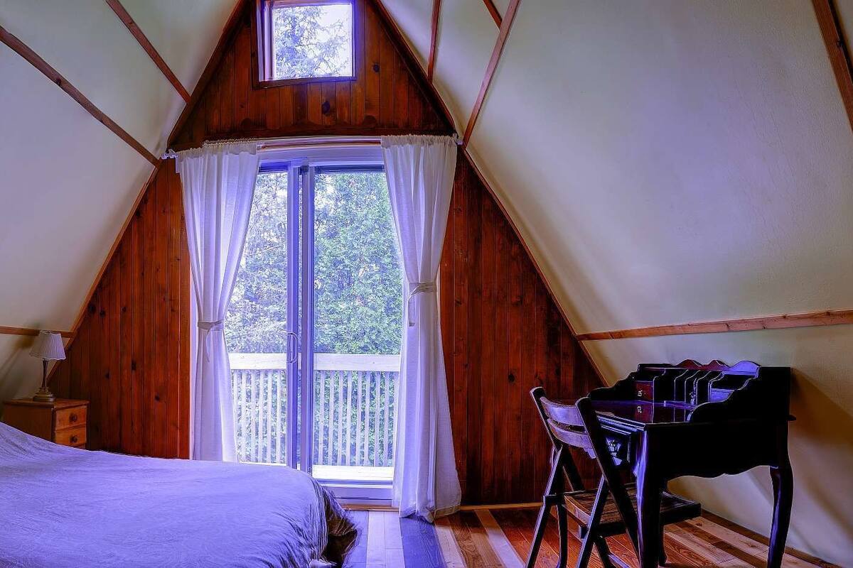 Ein gemütliches Schlafzimmer im Dachgeschoss mit einem Bett, einem Schreibtisch und einem Fenster mit Blick auf eine Holzterrasse.