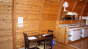 A wooden interior with a dining table and chairs, a kitchen area with a sink and stove, and a ceiling fan.