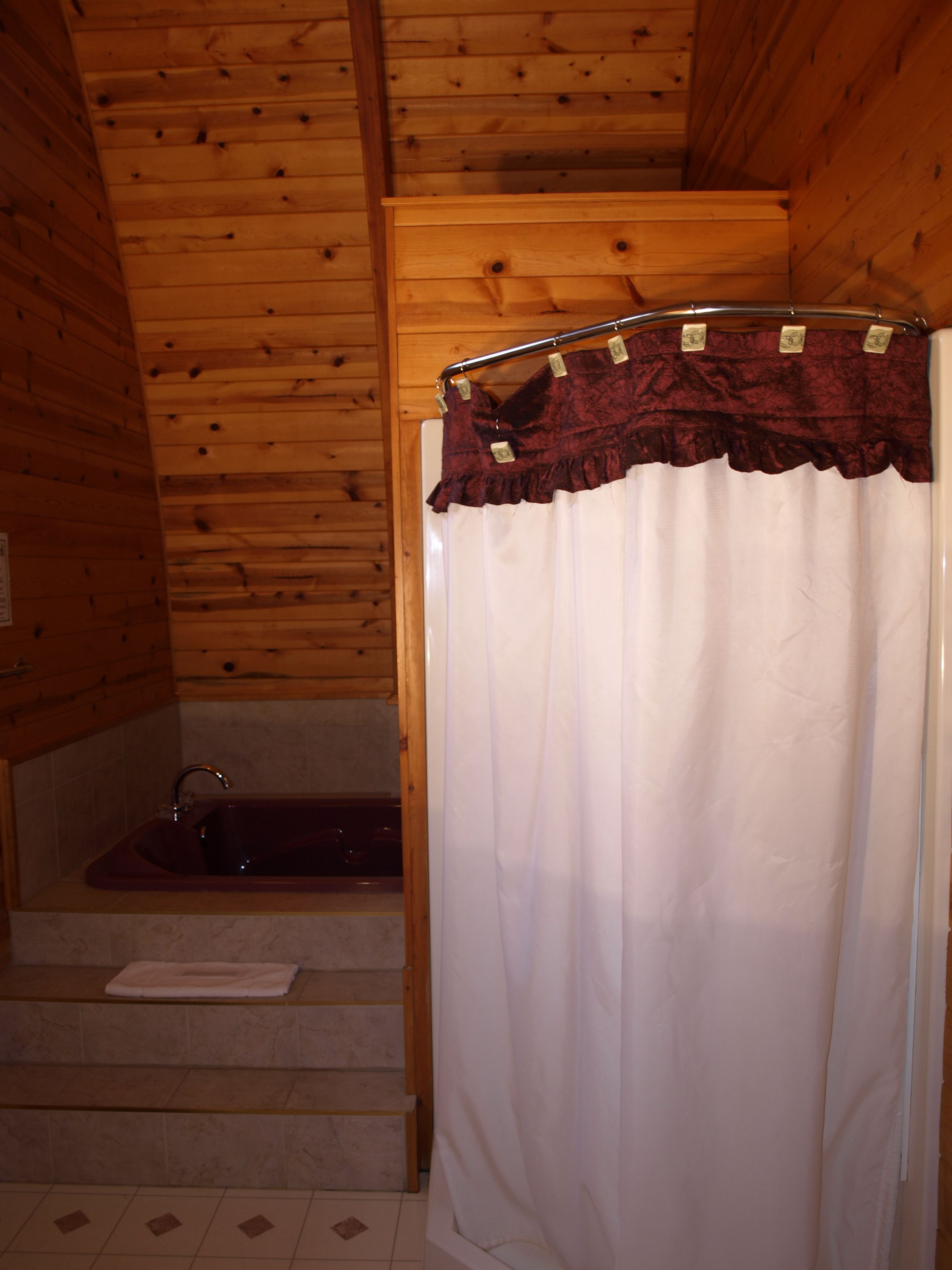 A wooden cabin bathroom with a bathtub, a shower curtain, and a set of stairs leading to the shower area.
