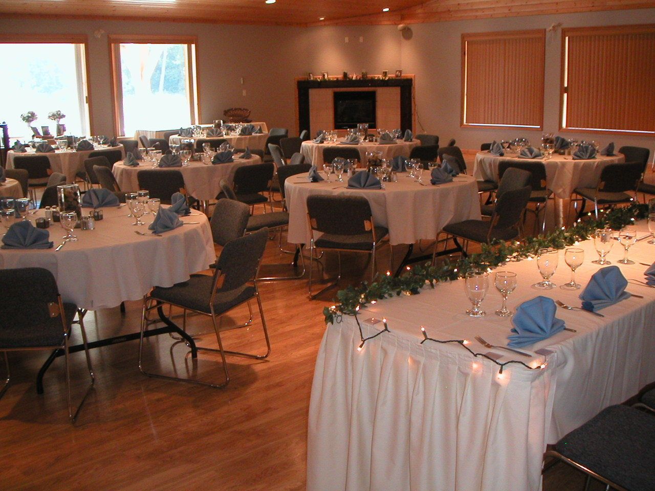 A banquet hall with round tables set for dining, chairs, and a fireplace.