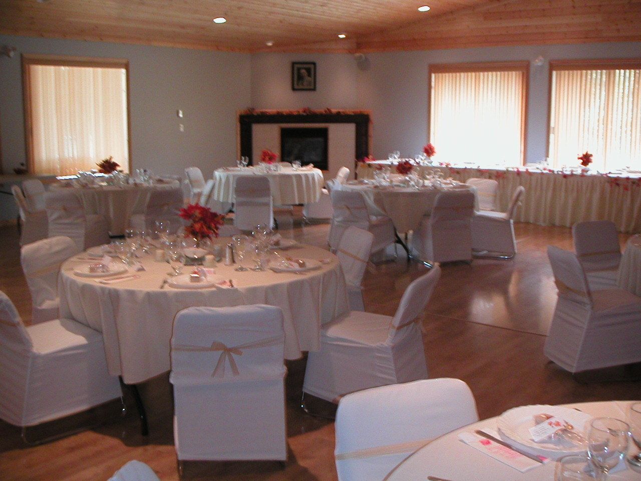 A banquet hall with round tables set for a formal event, white chairs, and a fireplace in the background.