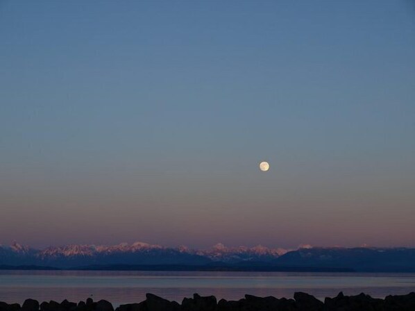 Una luna sobre un cuerpo de agua tranquilo con montañas al fondo.
