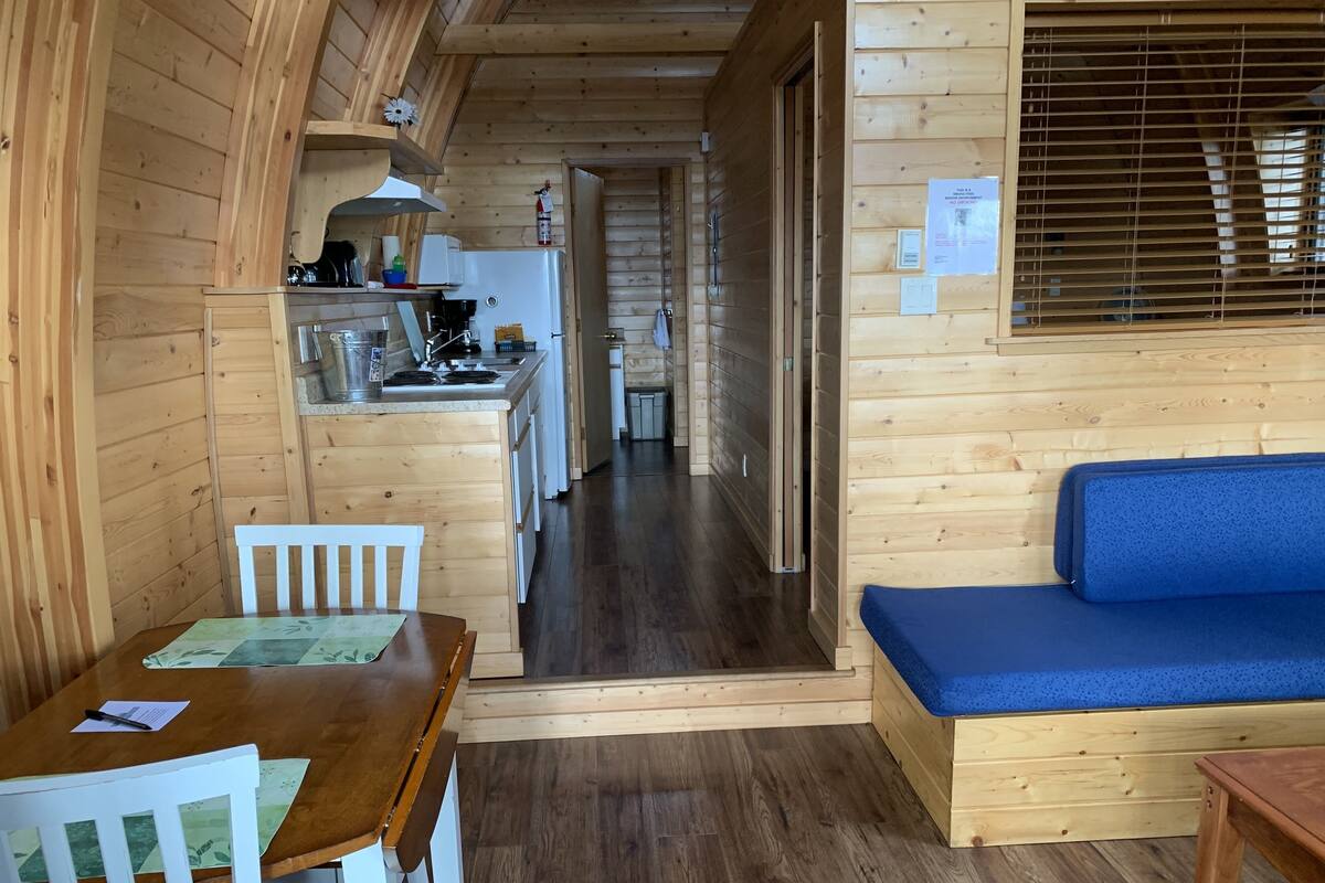 Een houten blokhut van binnen met een eethoek, kitchenette en een blauwe bank.