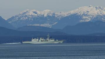 A military ship on calm waters with snow-capped mountains in the background.