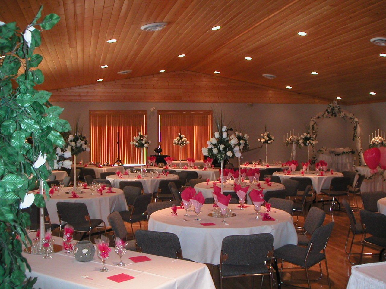 Une salle de banquet avec des tables rondes dressées pour le repas, agrémentées de nappes blanches et de serviettes roses.