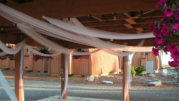 Un espacio al aire libre cubierto con vigas de madera y suelo de grava, rodeado por una cerca de madera y un edificio de ladrillo.