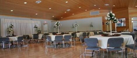 Un salón de conferencias con mesas redondas, sillas y centros de mesa con flores.