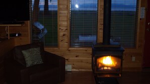 Un interior acogedor de cabaña con detalles de madera, una chimenea, un televisor montado en la pared y una ventana con vistas al exterior.