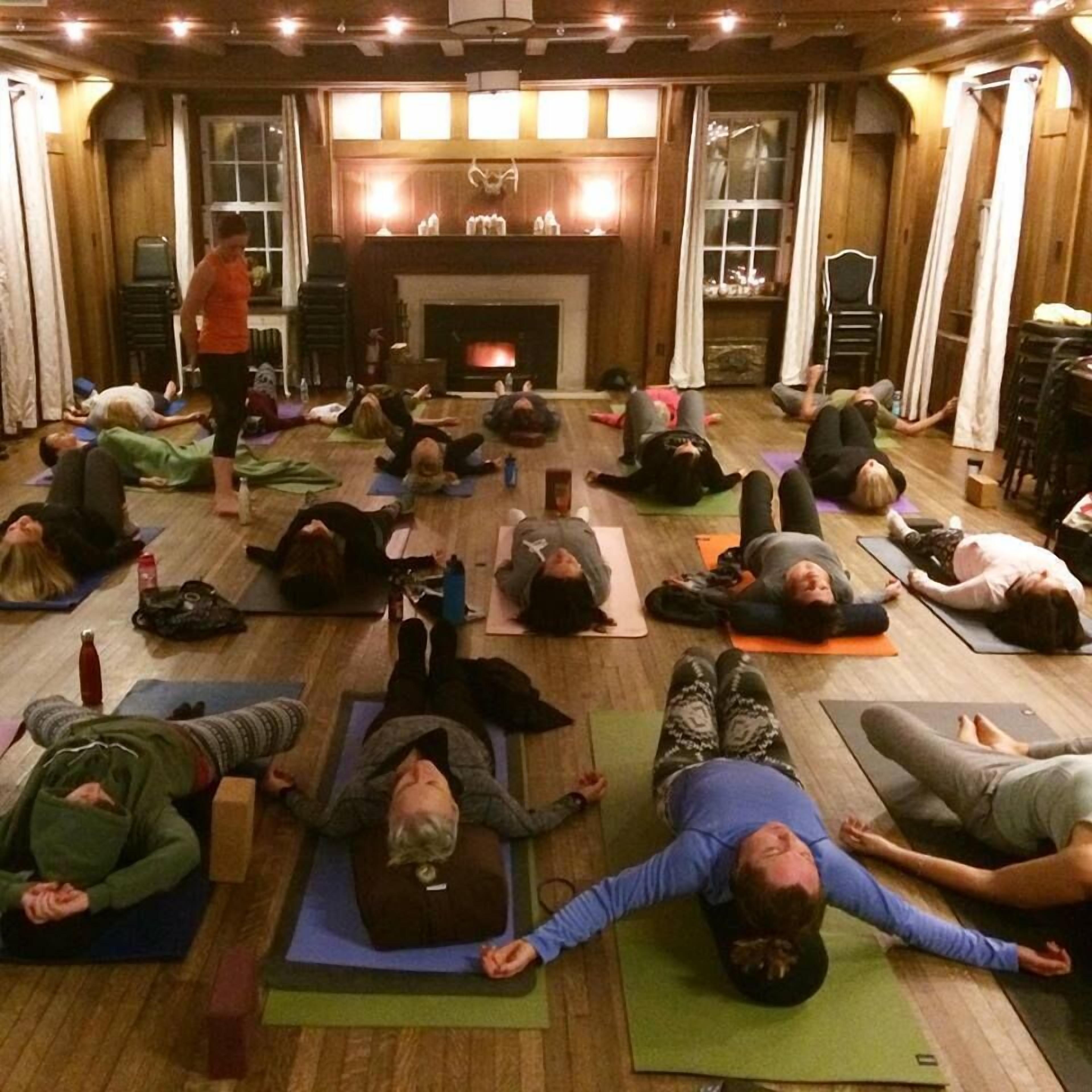 A group of people doing yoga in a spacious room with wooden floors and a fireplace.