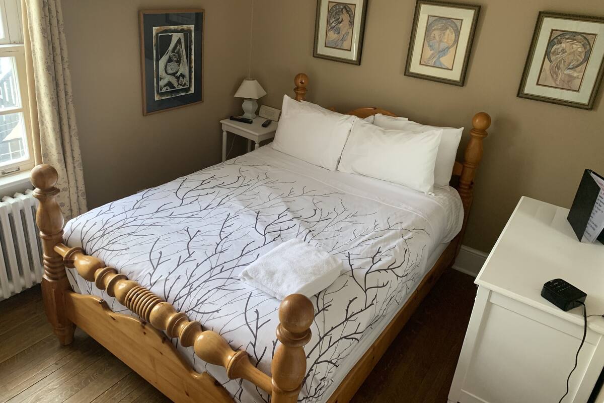 Una cama bien hecha con una colcha de diseño blanco y negro con motivos de árboles, un cabecero de madera y una mesita de noche con una lámpara y un control remoto.