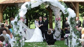 A gazebo wedding venue with a wooden roof, surrounded by guests seated on white chairs.