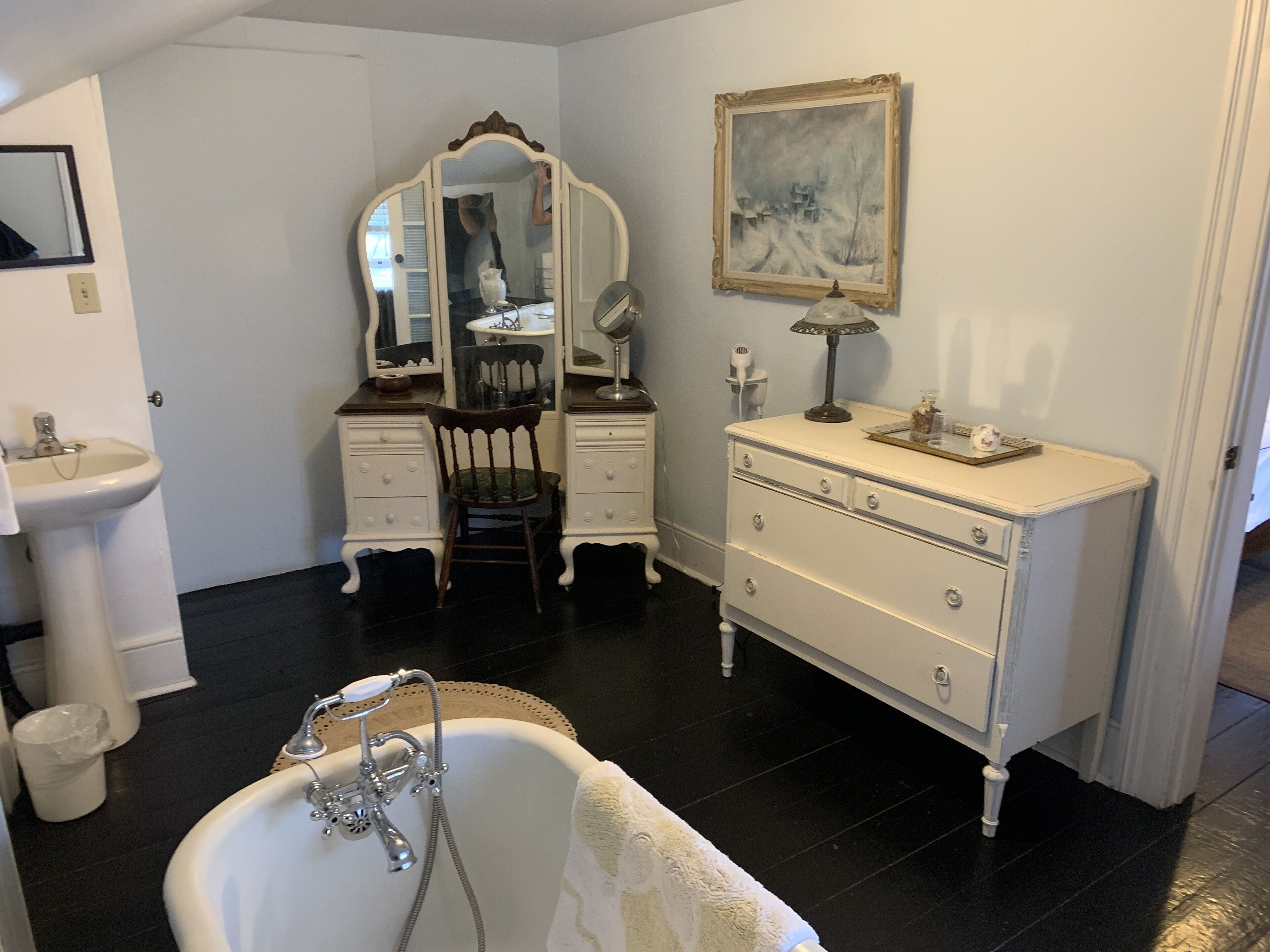 A bathroom with a white sink, a bathtub, a vanity with a mirror, and a painting on the wall.