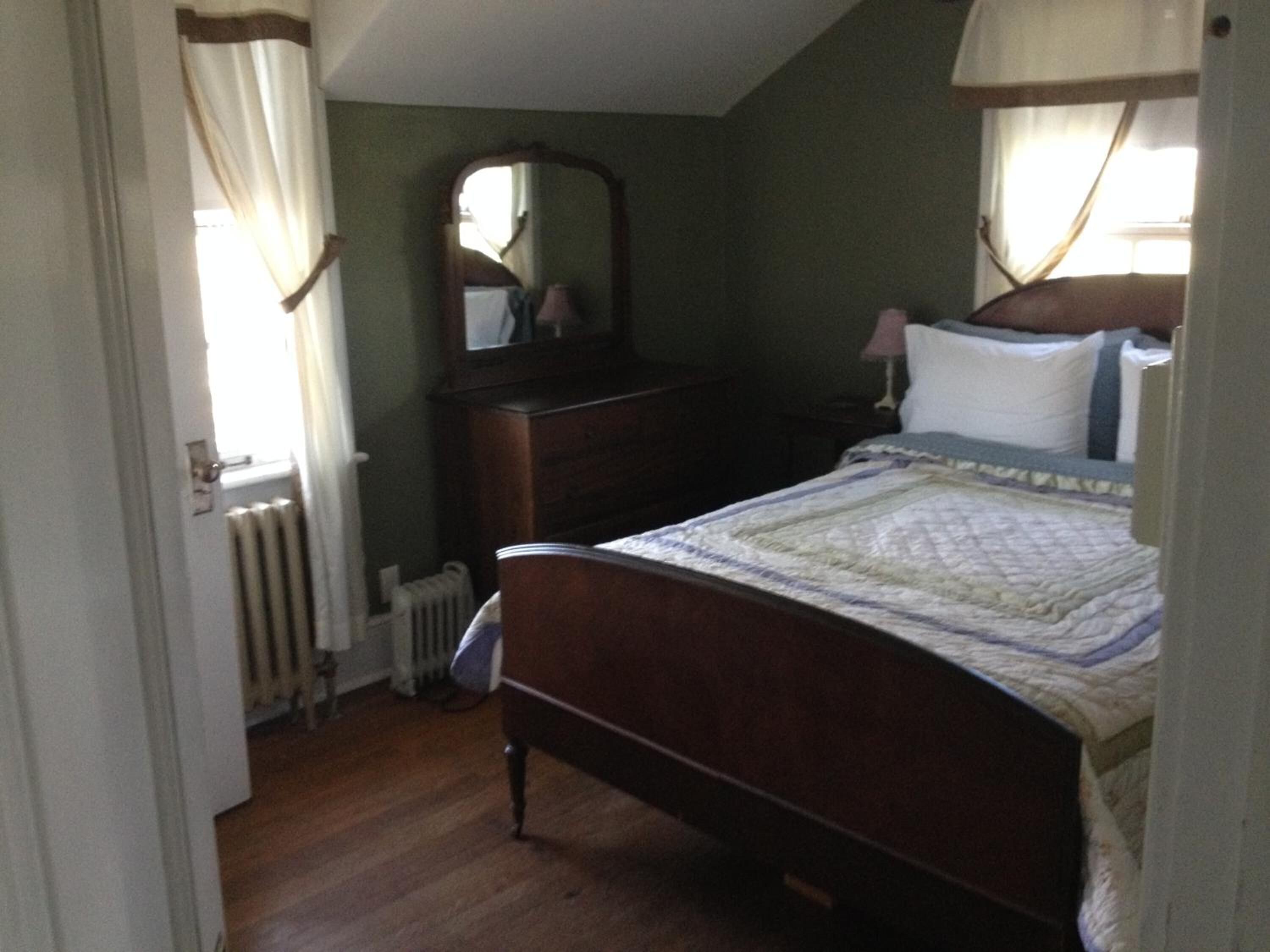 A bedroom with a wooden bed, a dresser, a mirror, and a radiator.
