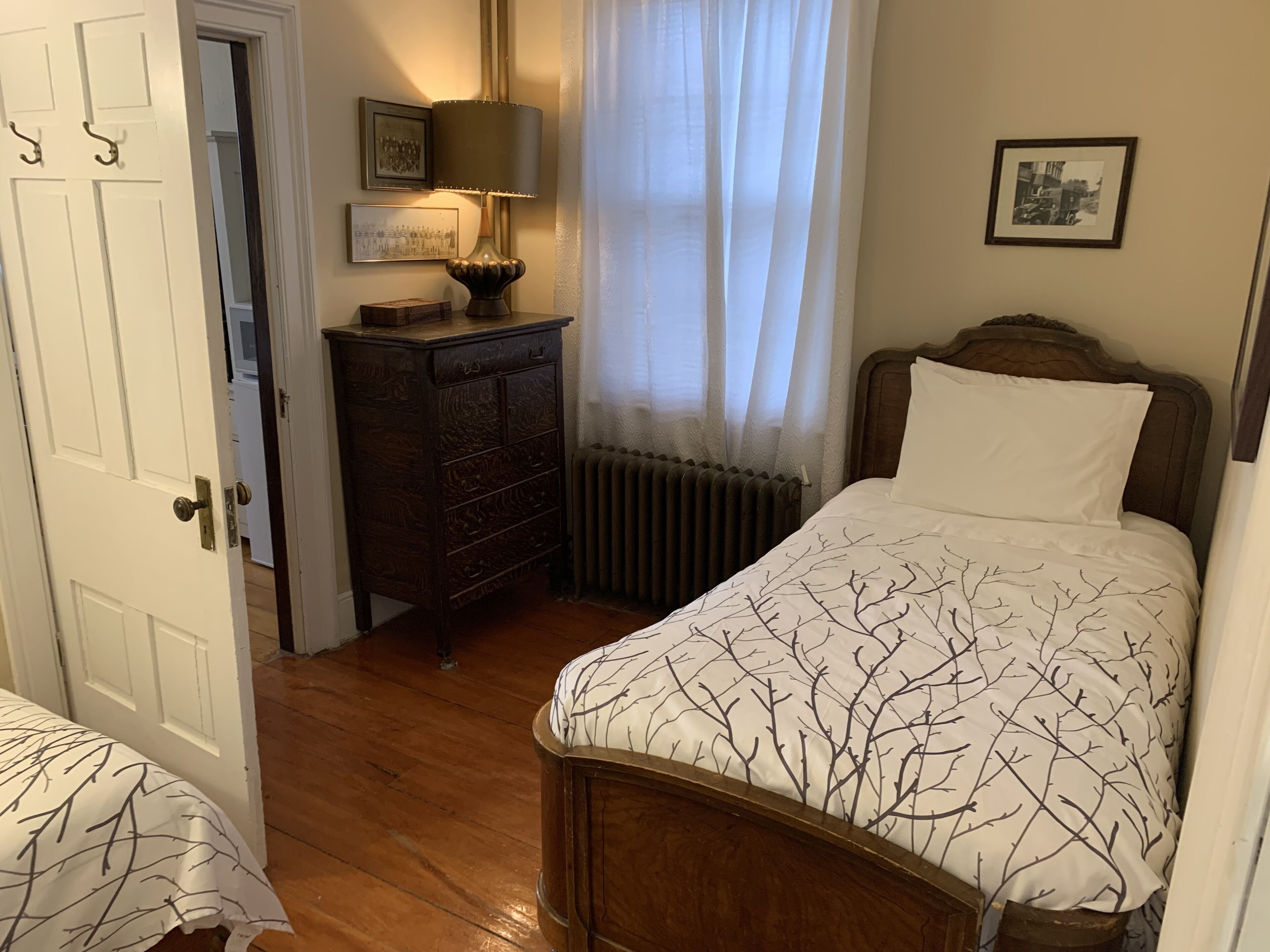 A bedroom with a wooden bed, a dresser, a lamp, and a radiator.